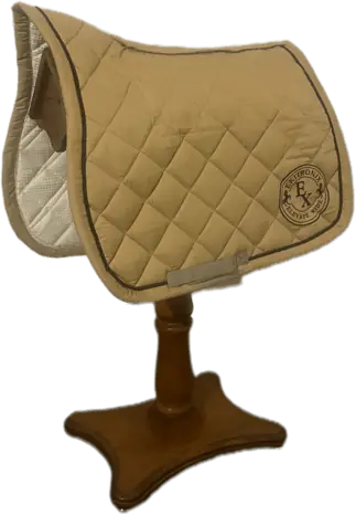 Le tapis Ekipad, beige et matelassé, passepoilé de brun et brodé du sceau Ekitronix, posé sur un porte-selle en bois.